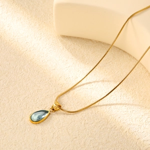 Close-up of golden snake chain with a blue teardrop pendant on a minimalist display