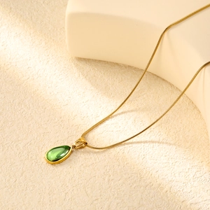 Detail of a vintage gold necklace with a green water drop stone pendant on beige prop