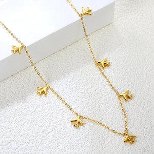 Detail view of gold airplane pendant necklace with multiple charms on white texture