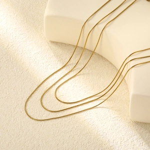 Minimalist three-layer golden snake chain necklaces draped on a white geometric prop