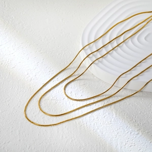 Minimalist three-layer gold snake bone chain necklace on an elegant white textured base