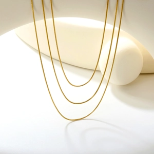 Three-layer gold snake bone chain necklaces displayed on minimalist white geometric props