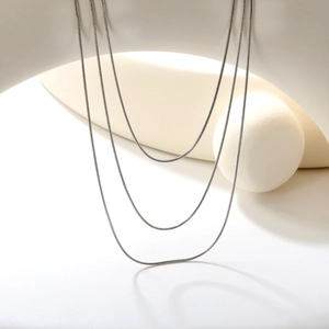 Detailed view of layered silver snake chains draped elegantly over a minimalist white display