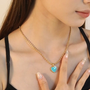 Collier à billes dorées avec pendentif cœur en émail bleu porté par un mannequin