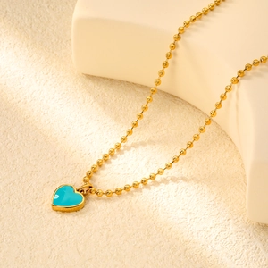 Gros plan d'une chaîne à billes dorée avec pendentif cœur émaillé bleu turquoise