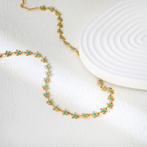 Collier doré minimaliste avec marguerites et perles turquoise sur fond blanc