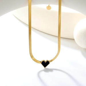 Collier chaîne serpent dorée avec pendentif cœur noir sur présentoir géométrique blanc
