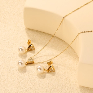 Detailed view of gold pearl necklace and heart stud earrings set on a warm beige background