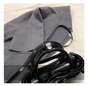 Détail d'un sac à main noir brillant avec poignées rondes et rivets en métal