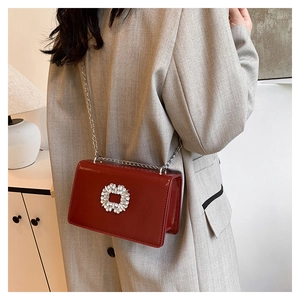 Detail of red rhinestone square bag with chain strap worn on a gray blazer jacket