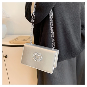 Detail of silver metallic handbag featuring a square rhinestone buckle and double chain strap