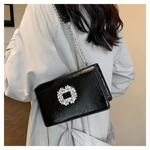 Detail of black patent leather crossbody bag with square rhinestone buckle and silver chain