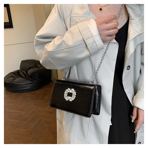 Detail view of the elegant black shoulder bag featuring a sparkling crystal square buckle.
