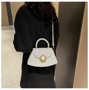 Detail der weißen Handtasche mit Krokodilprägung und goldener Schließe auf schwarzer Kleidung