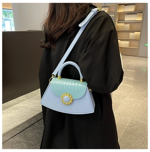 Detail der hellblauen Kroko-Handtasche mit goldenem Sonnenverschluss und Gurt