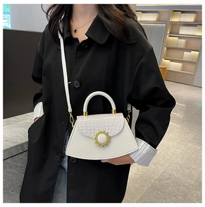 Detail der weißen Krokodilprägung mit goldenem Sonnenblumen-Verschluss an Handtasche