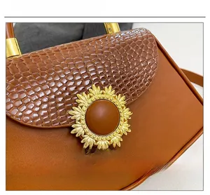 Detailaufnahme des goldenen Sonnenblumen-Beschlags an der Krokostruktur-Box-Tasche