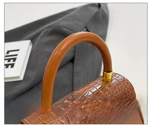 Detail der braunen Krokodilmuster-Handtasche mit rundem Griff und goldenen Metallschnallen