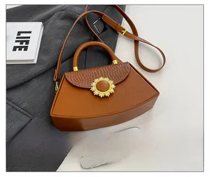 Detail einer braunen Trapez-Handtasche mit Krokostruktur und goldener Sonnenblumen-Schließe