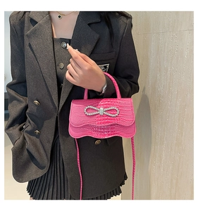 Detail of pink crocodile embossed bag with rhinestone bow and wavy flap design