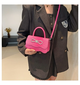 Detailed view of pink crocodile pattern handbag with sparkling rhinestone bow on grey blazer