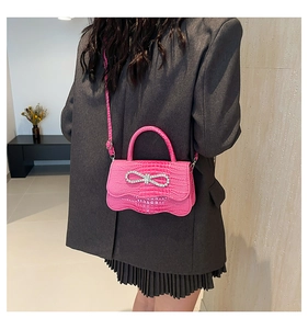 Detail of rose pink crocodile embossed handbag with rhinestone bow on grey blazer
