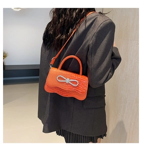 Crocodile pattern orange handbag featuring a large rhinestone bow buckle and top handle