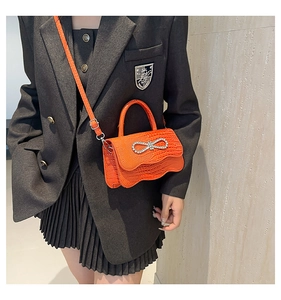Crossbody view of bright orange crocodile pattern handbag with crystal bow decoration