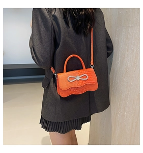 Detailed view of orange crocodile-pattern handbag with rhinestone bow on charcoal suit