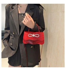 Close-up of red crocodile embossed handbag with sparkling rhinestone bow detail