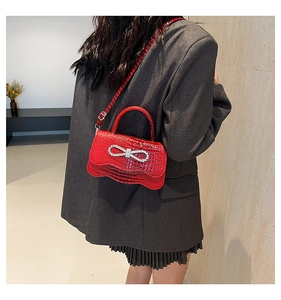 Detail of red croc-effect handbag featuring a sparkling rhinestone bow and wavy bottom design