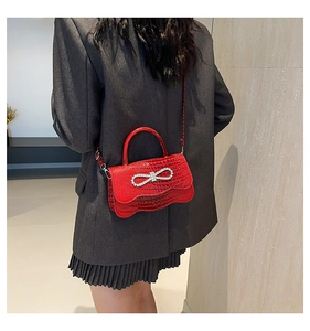 Detail of red crocodile texture handbag with crystal bow on grey blazer background