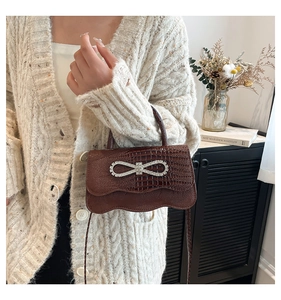 Detail of brown crocodile pattern handbag with sparkling crystal bow and wavy flap edge