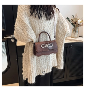 Detail of dark brown crocodile texture handbag with crystal bow on a model outfit