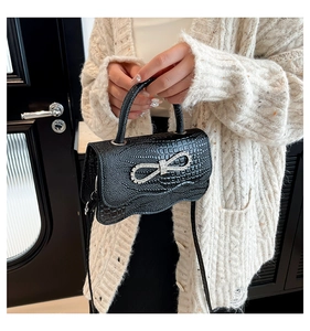 Detail of black crocodile pattern handbag featuring a sparkling rhinestone bow buckle