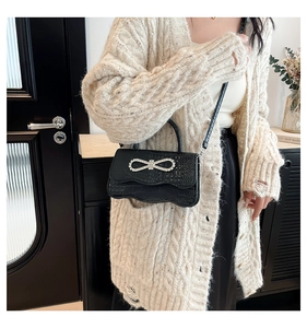 Close-up of black crocodile texture handbag with sparkling silver rhinestone bow detail