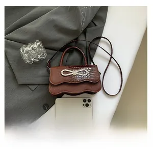 Detail of crocodile textured brown handbag with rhinestone bow and mobile phone for scale