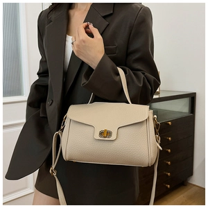 Détail du sac à bandoulière en cuir grainé beige avec fermoir doré porté par le mannequin