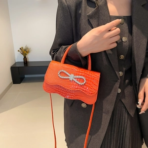 Orange crocodile texture handbag with rhinestone bow decoration worn by female model