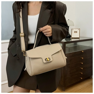 Détail d'un sac à main beige en cuir grainé avec fermoir doré sur une veste en cuir sombre