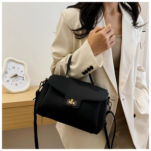 Détail du sac à main noir en cuir grainé avec fermoir doré porté sur un blazer beige chic