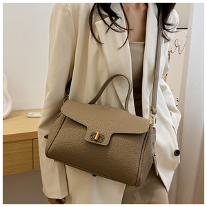 Sac à main en cuir kaki avec fermoir doré porté sur un blazer de couleur crème