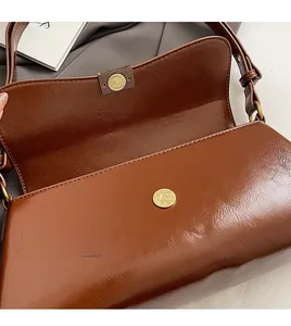 Detail of a brown leather shoulder bag featuring a gold magnetic snap button closure