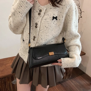 Borsa baguette vintage nera con chiusura dorata indossata su un cardigan beige
