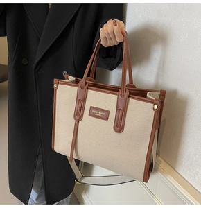 Detail view of large canvas tote bag with brown leather trim and fashion brand tag