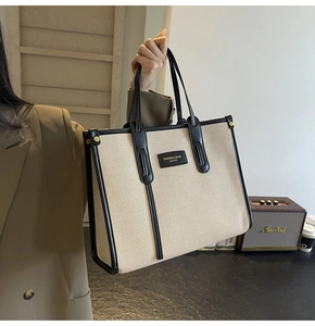 Detailed view of canvas tote bag with black leather trim held by a model in a cozy room