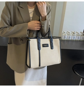 Close-up of canvas tote bag with black leather trim and embossed fashion label