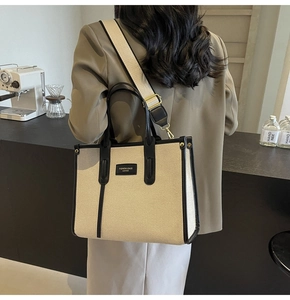 Detail of model wearing a beige canvas tote bag with black leather trim and wide strap