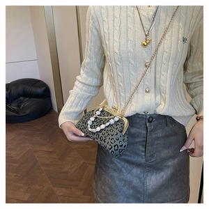 Detail of leopard print shell bag featuring pearl handle and gold chain on model