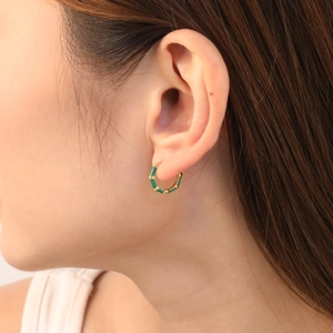 Bamboo shaped gold hoop earrings with dark green enamel detail worn by a model
